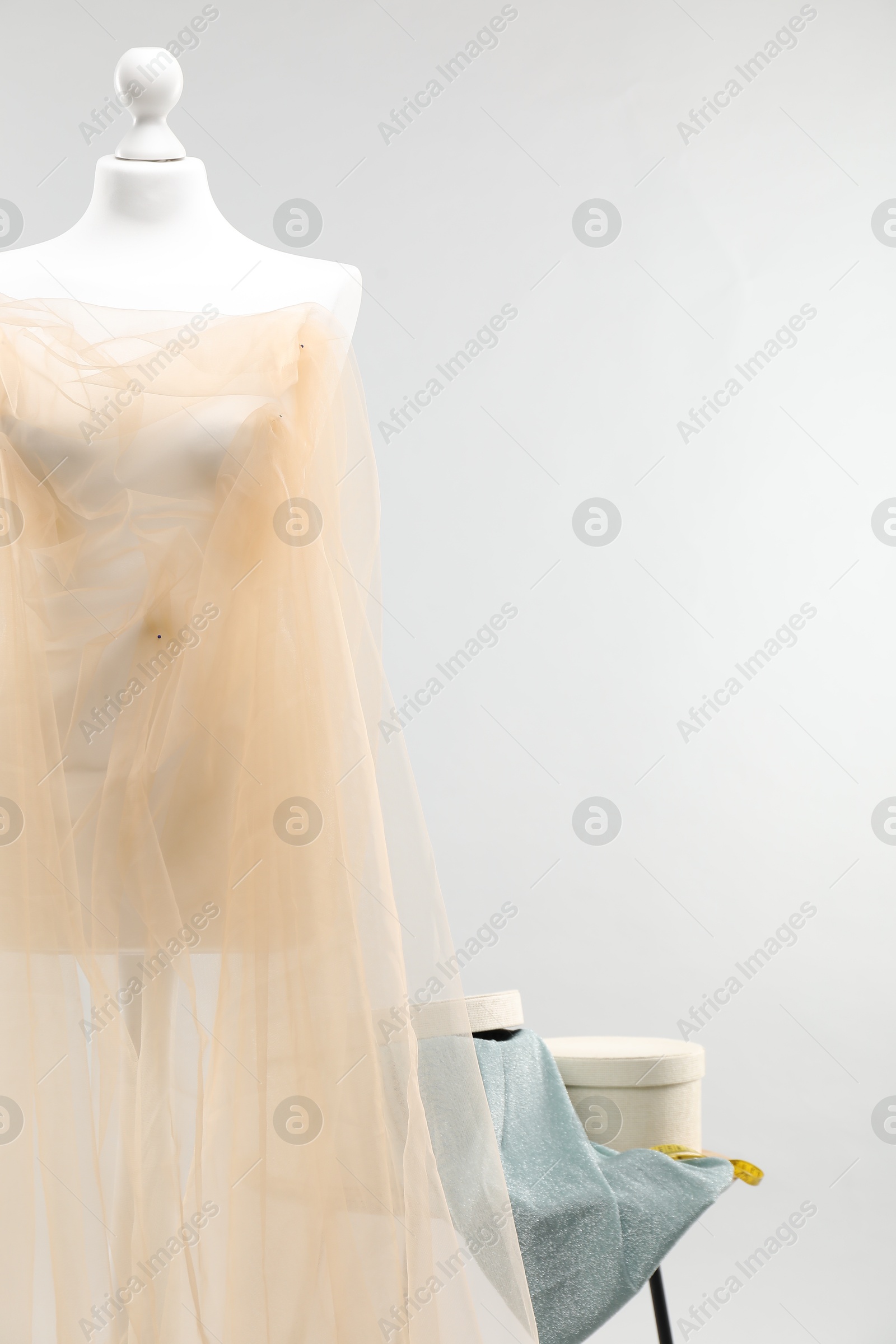 Photo of Mannequin with fabric and boxes on side table against light grey background. Creating new outfit