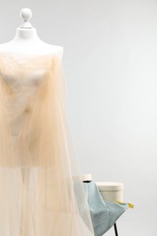 Photo of Mannequin with fabric and boxes on side table against light grey background. Creating new outfit