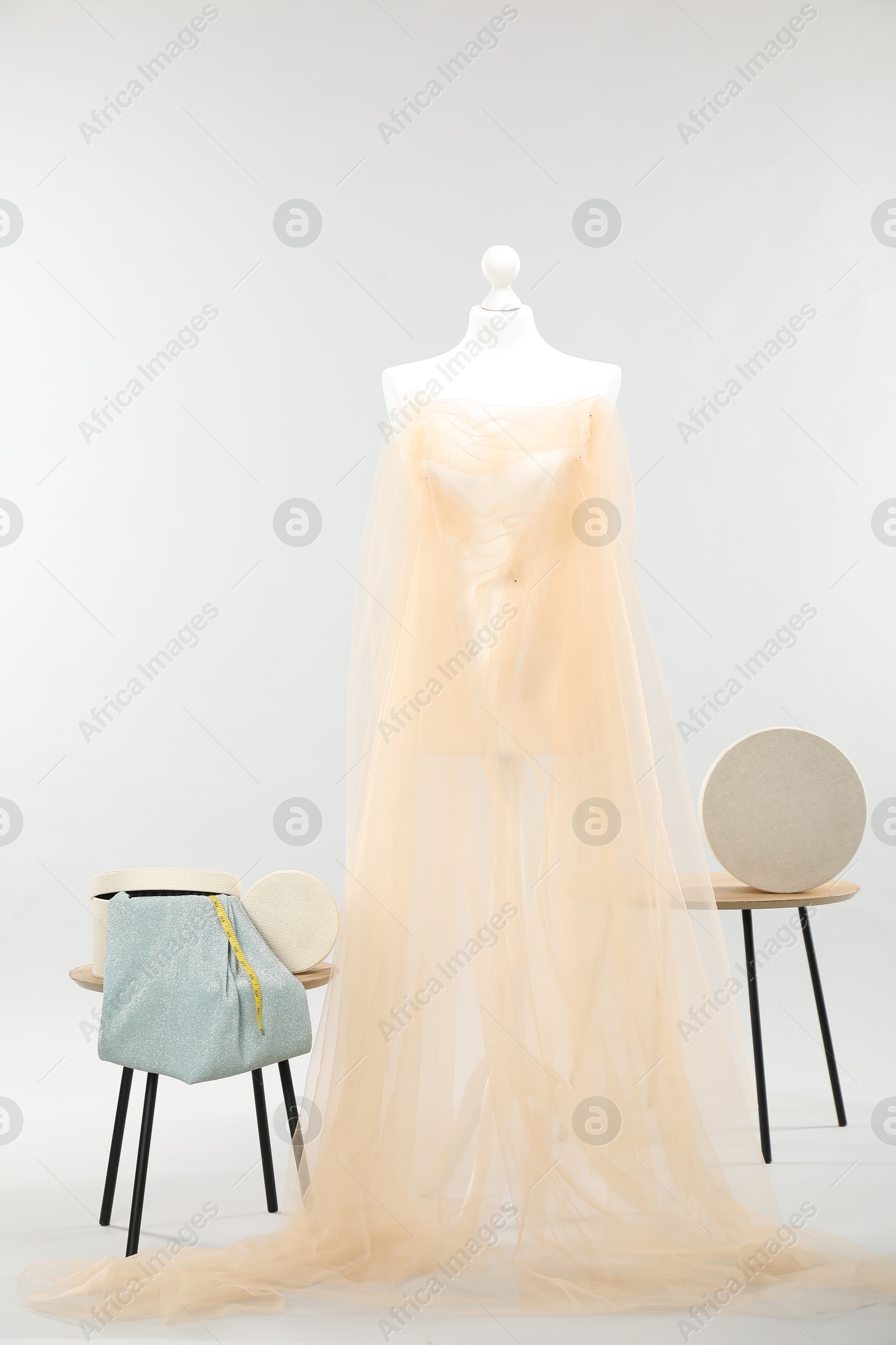 Photo of Mannequin with fabric and boxes on side tables against light grey background. Creating new outfit