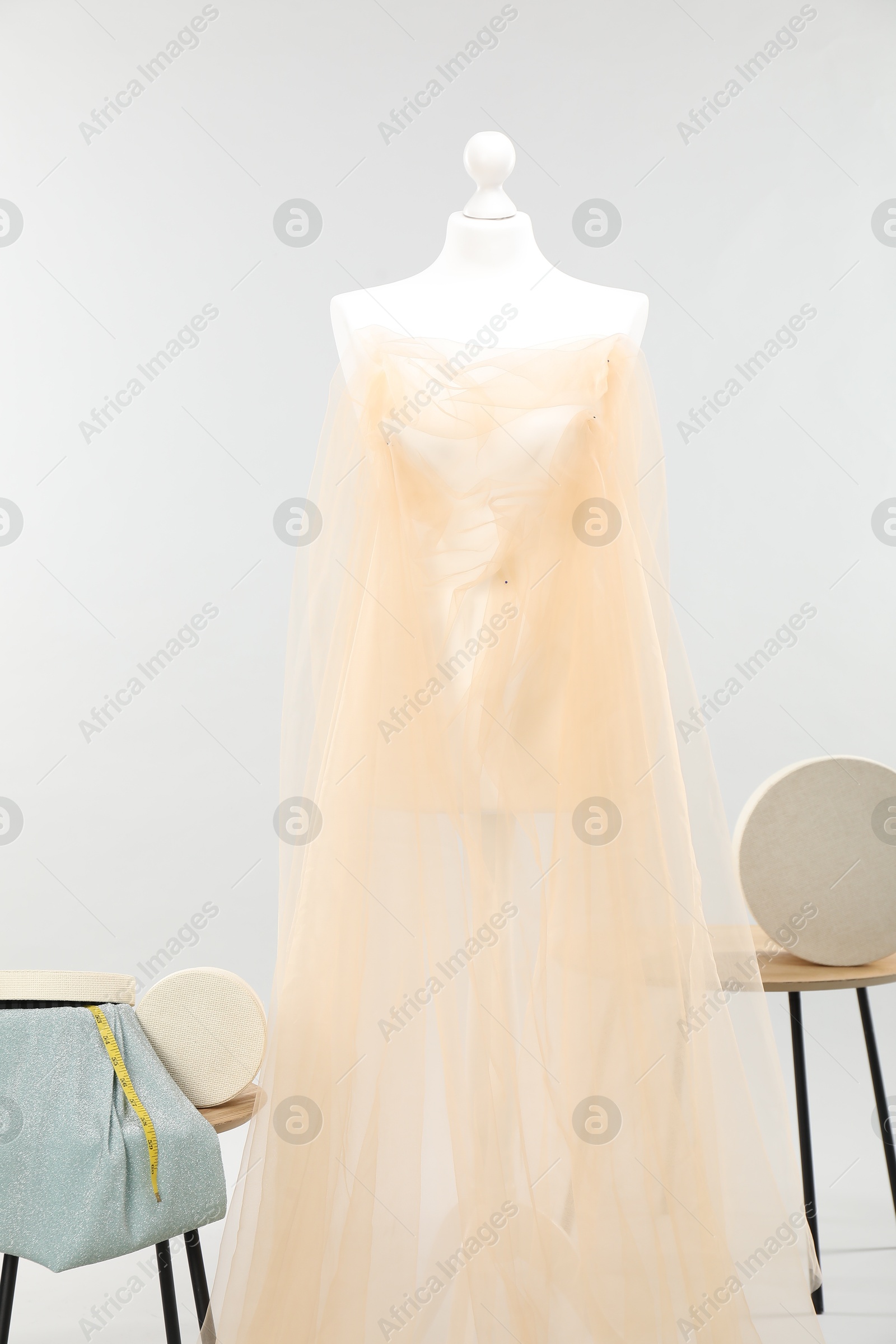 Photo of Mannequin with fabric and boxes on side tables against light grey background. Creating new outfit