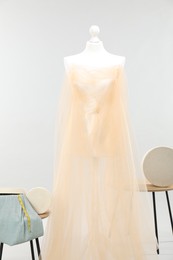 Photo of Mannequin with fabric and boxes on side tables against light grey background. Creating new outfit