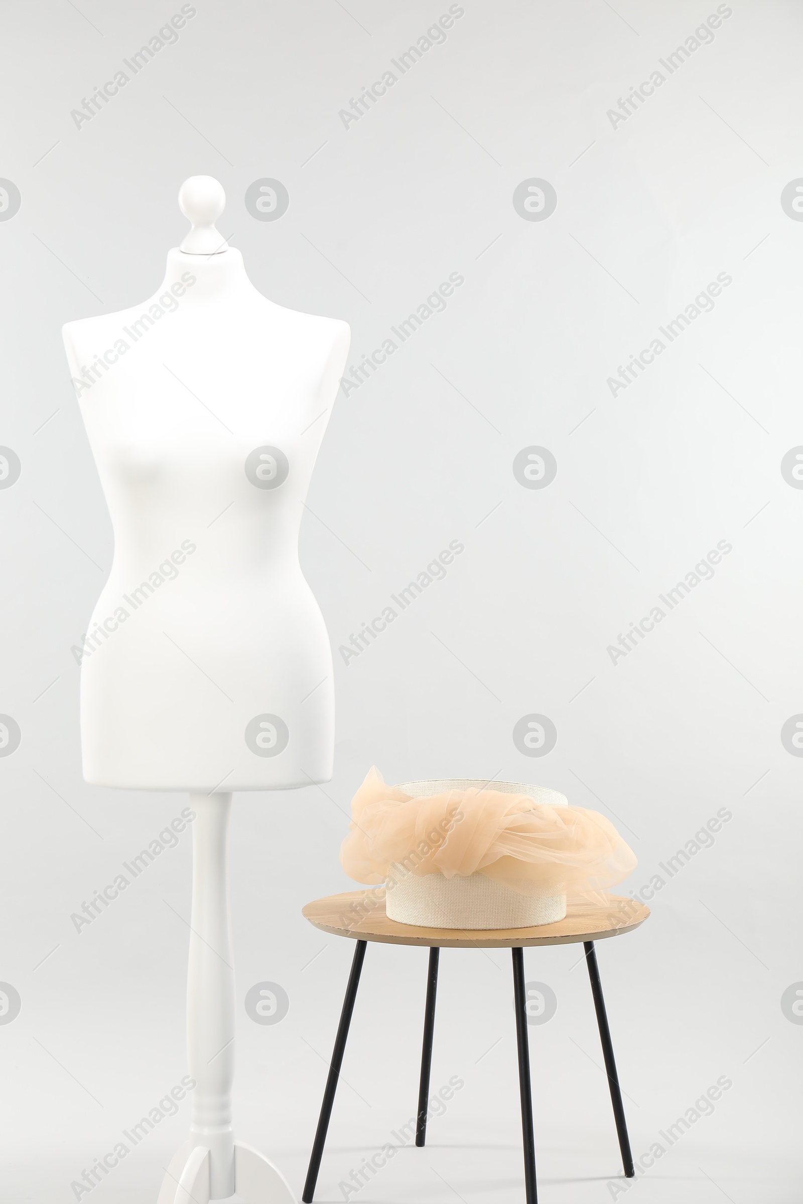 Photo of Mannequin with box of fabric on side table against light grey background. Creating new outfit