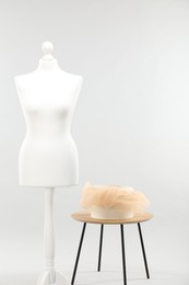 Mannequin with box of fabric on side table against light grey background. Creating new outfit