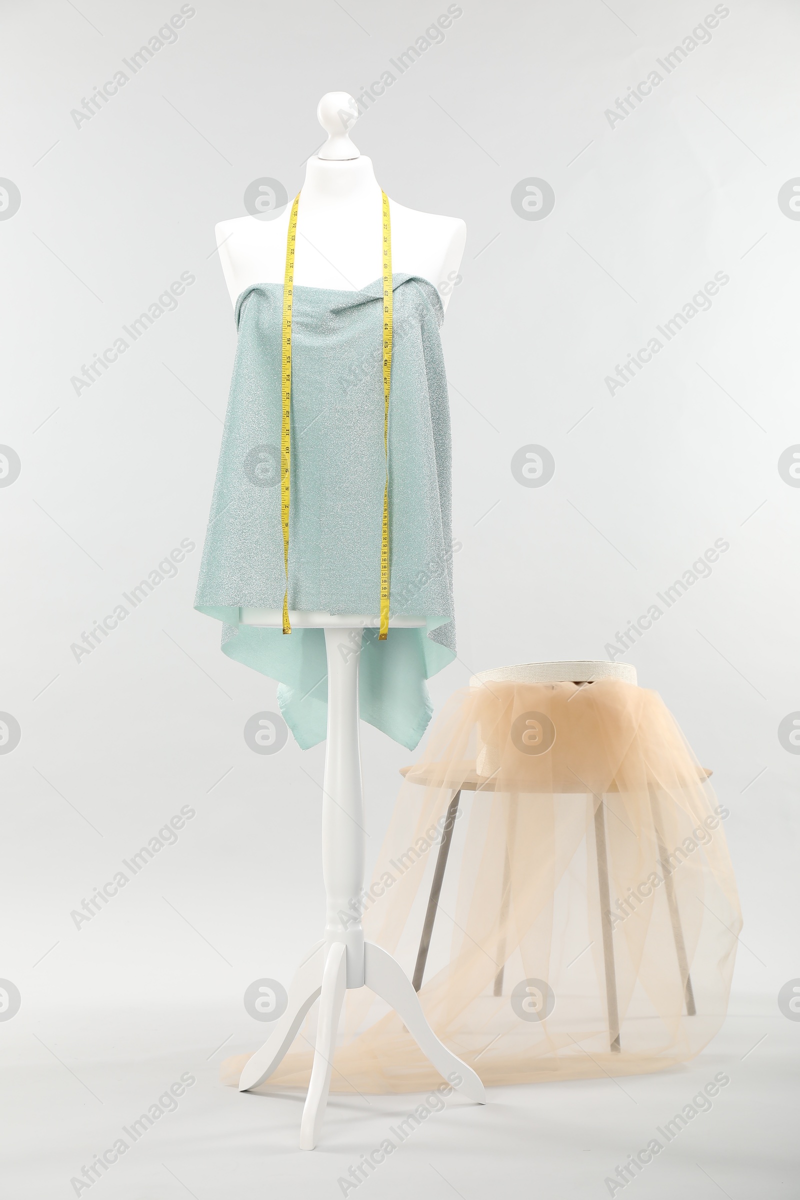 Photo of Mannequin with measuring tape, fabric and box on side table against light grey background. Creating new outfit