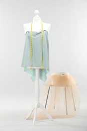 Photo of Mannequin with measuring tape, fabric and box on side table against light grey background. Creating new outfit