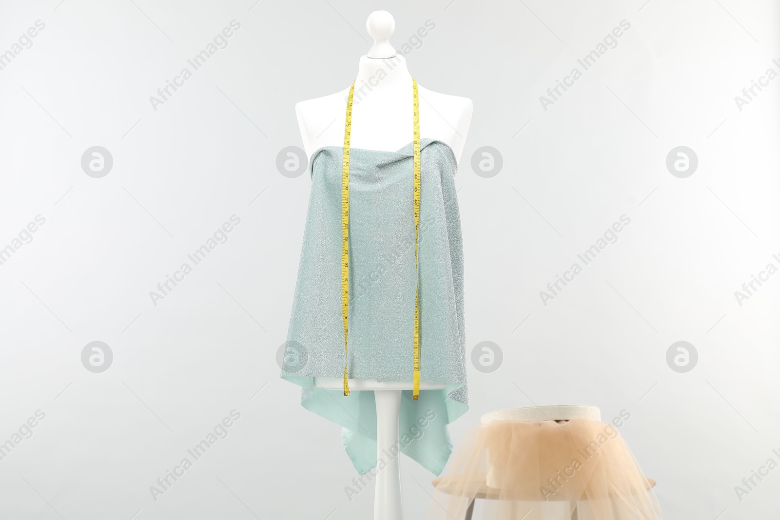 Photo of Mannequin with measuring tape, fabric and box on side table against light grey background. Creating new outfit