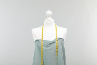 Photo of Mannequin with measuring tape and fabric against light grey background. Creating new outfit