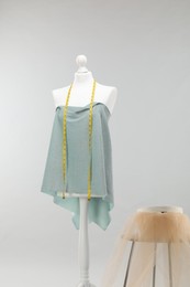 Photo of Mannequin with measuring tape, fabric and box on side table against light grey background. Creating new outfit