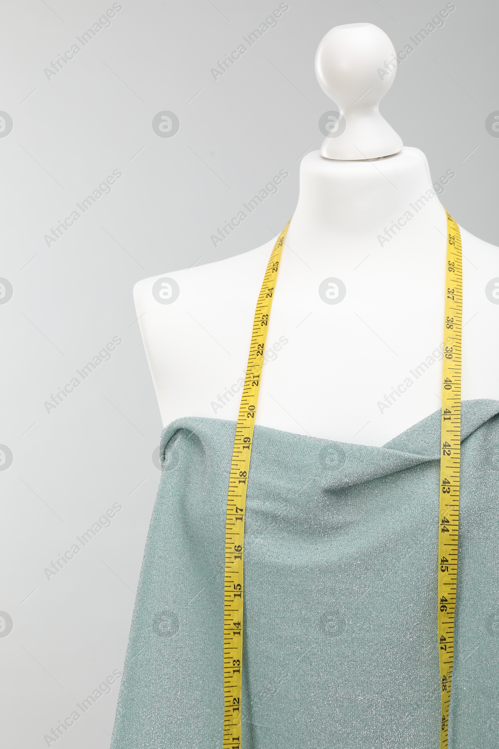 Photo of Mannequin with measuring tape and fabric against light grey background. Creating new outfit