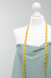 Photo of Mannequin with measuring tape and fabric against light grey background. Creating new outfit