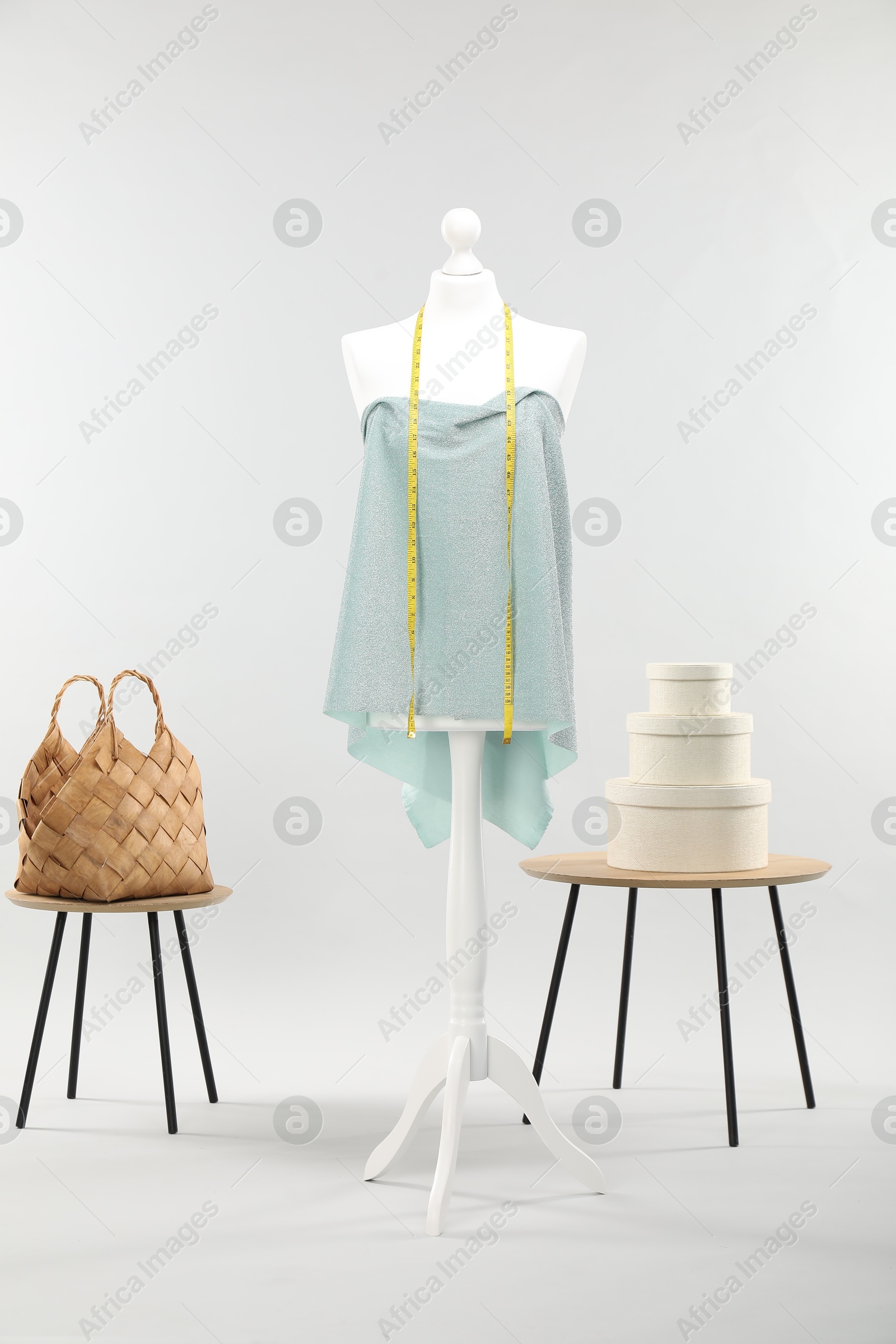 Photo of Mannequin with measuring tape, fabric, bag and boxes on side tables against light grey background. Creating new outfit