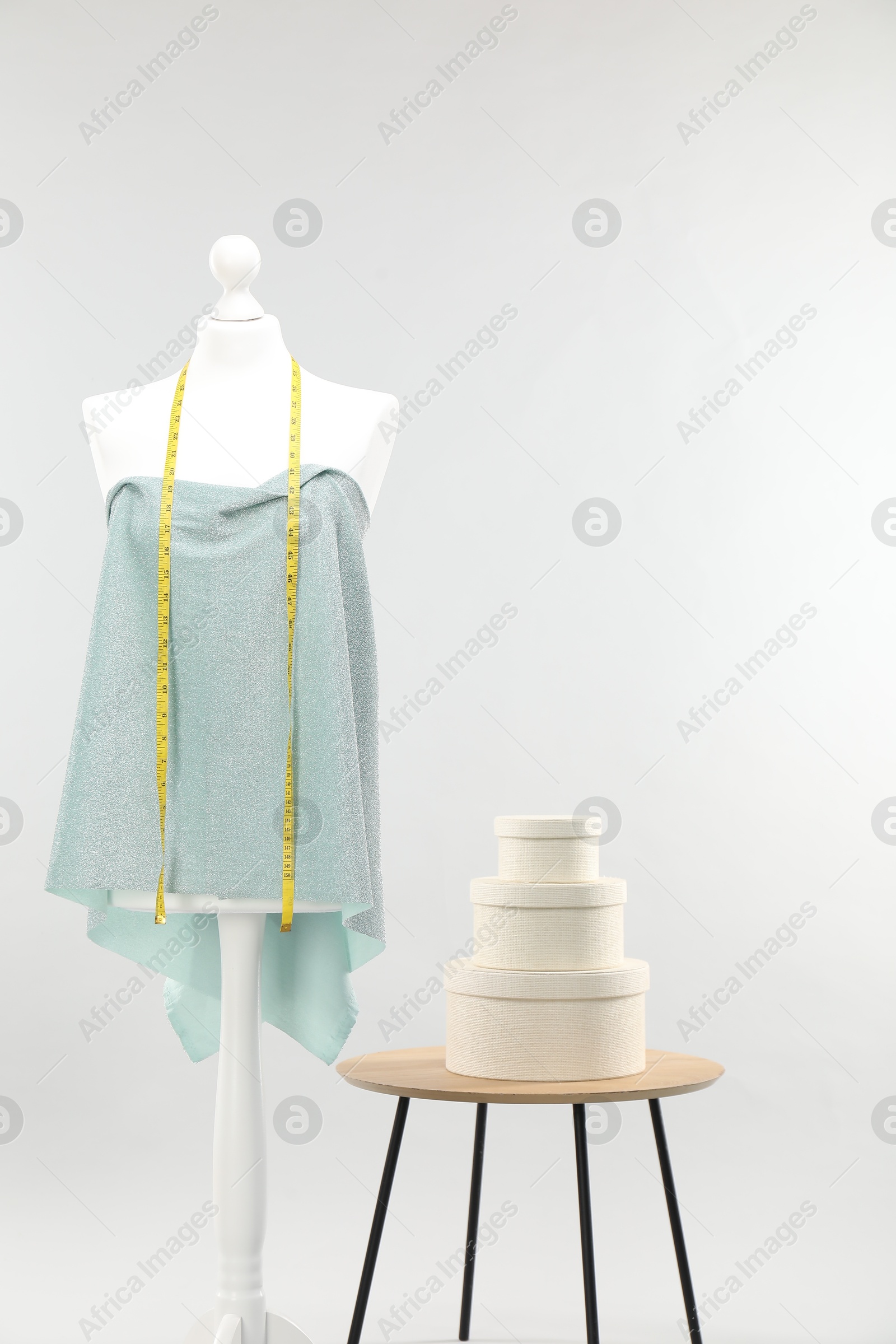 Photo of Mannequin with measuring tape, fabric and boxes on side table against light grey background. Creating new outfit