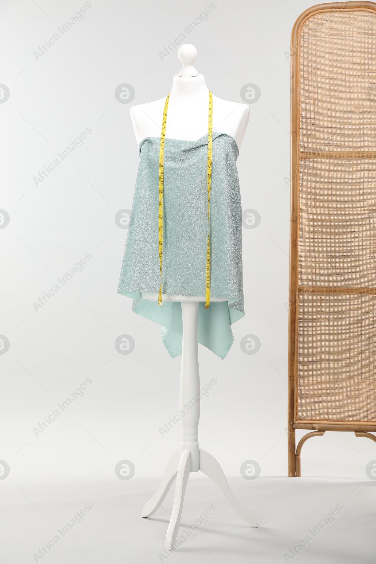 Photo of Mannequin with measuring tape and fabric against light grey background. Creating new outfit