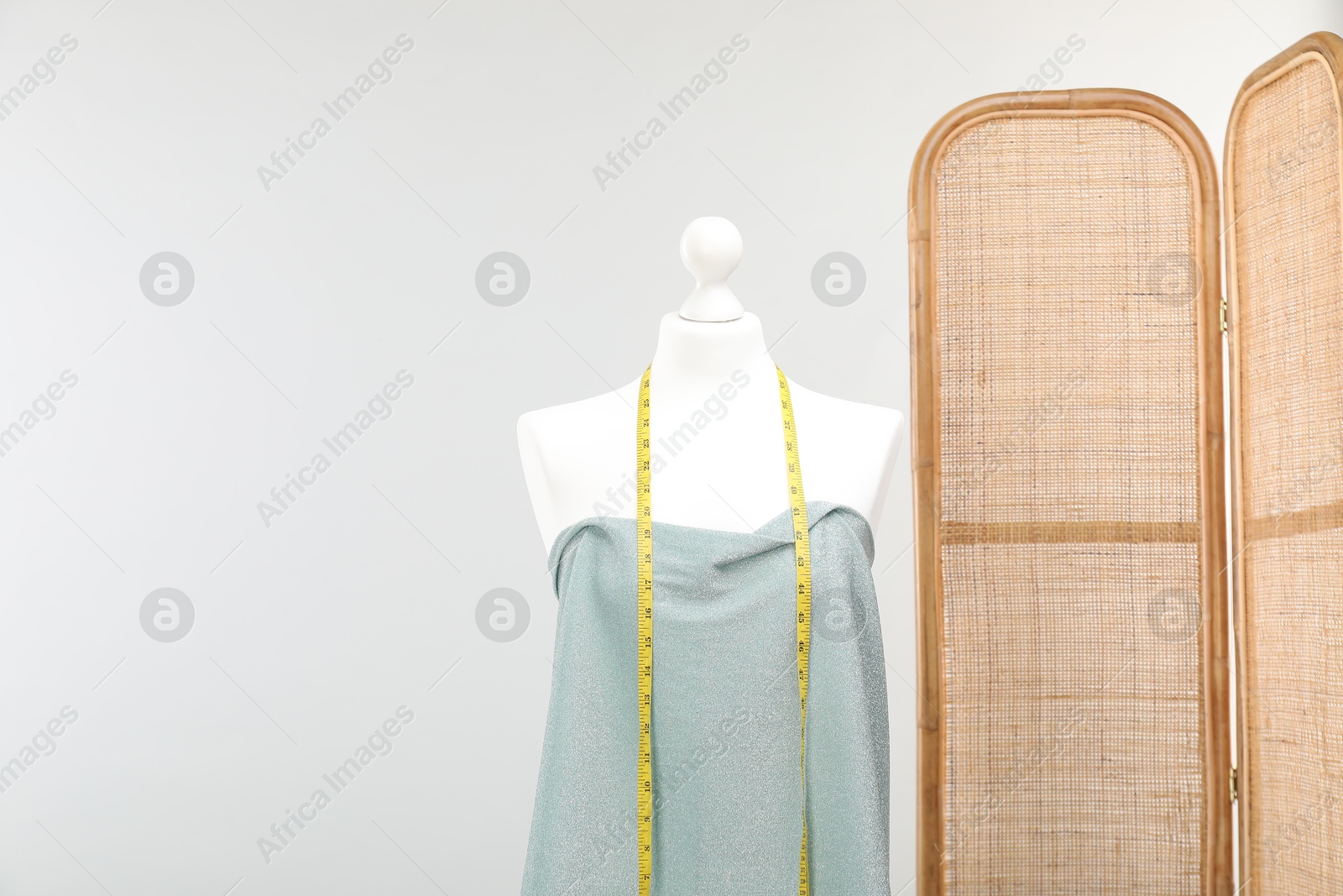 Photo of Mannequin with measuring tape and fabric against light grey background. Creating new outfit