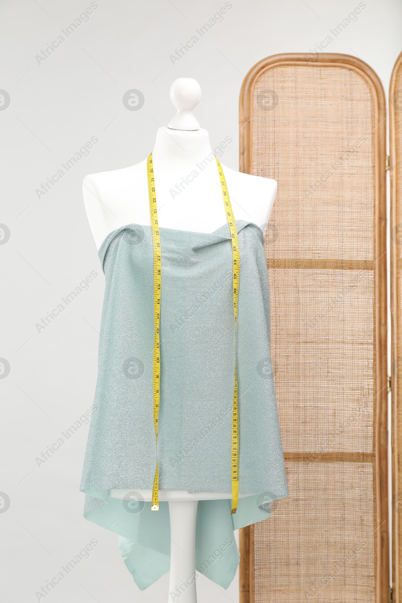 Photo of Mannequin with measuring tape and fabric against light grey background. Creating new outfit