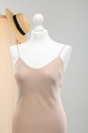 Photo of Mannequin with new stylish dress and wicker hat against light grey background