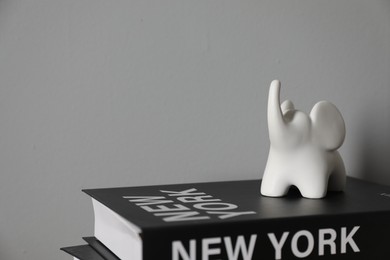 Book with words New York written on cover and ceramic elephant figure near gray wall, closeup. Space for text