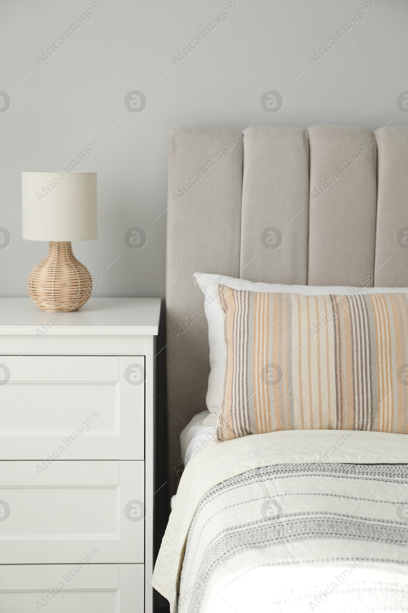 Photo of Comfortable bed with soft pillows and lamp on white bedside table in bedroom