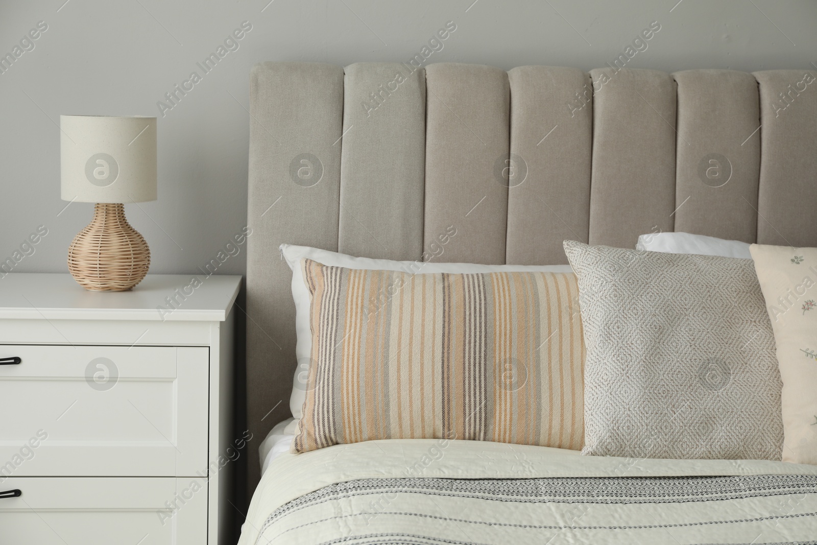 Photo of Comfortable bed with soft pillows and lamp on white bedside table in bedroom