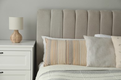 Photo of Comfortable bed with soft pillows and lamp on white bedside table in bedroom