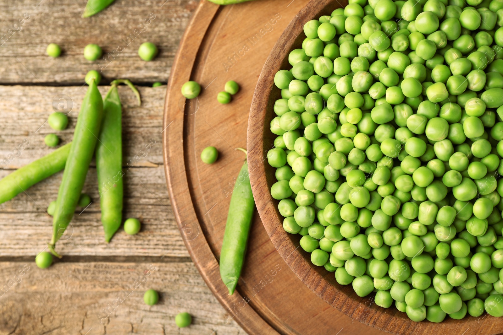 Photo of Fresh green peas in bowl and pods on wooden table, flat lay