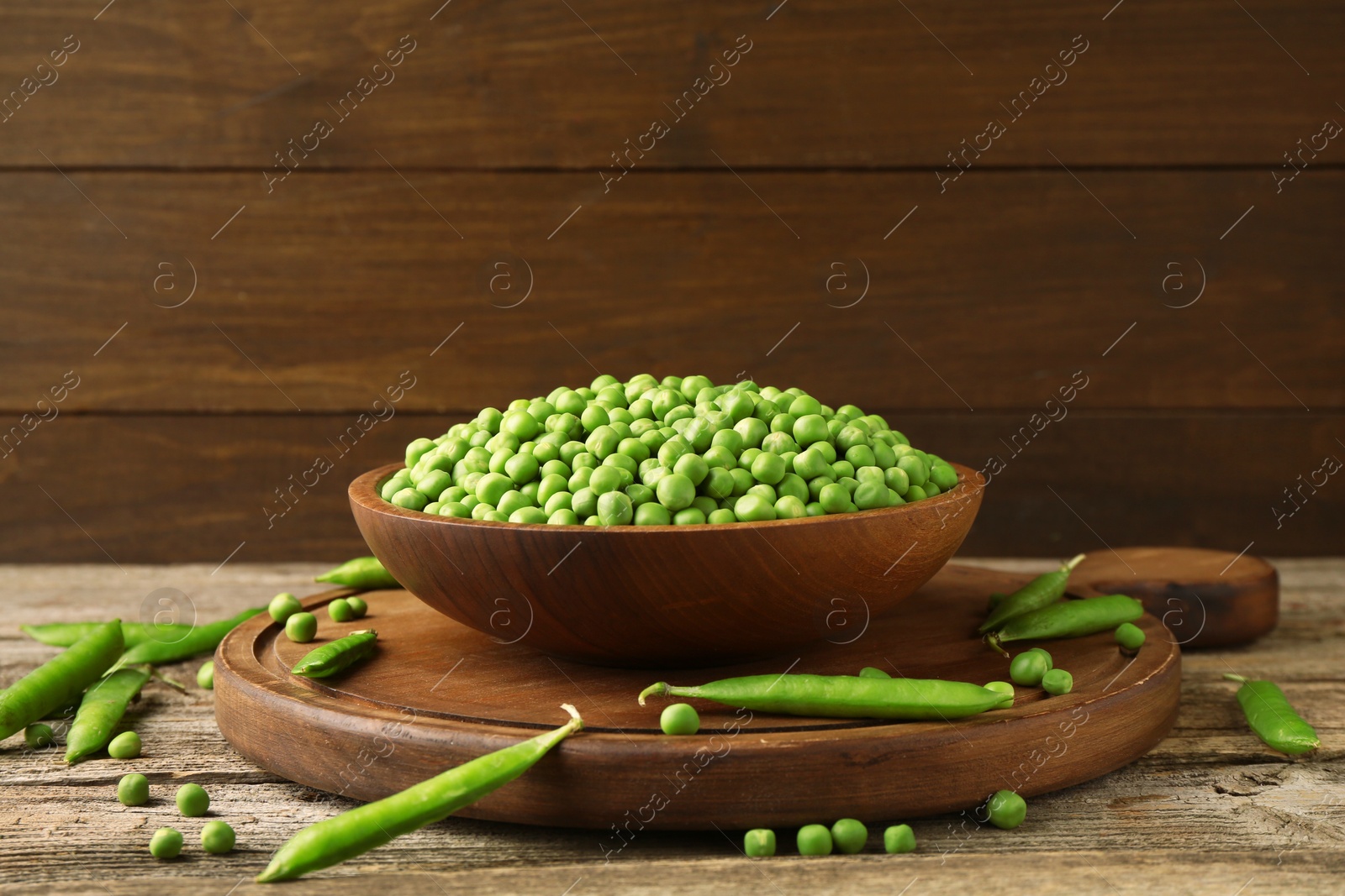 Photo of Fresh green peas in bowl and pods on wooden table