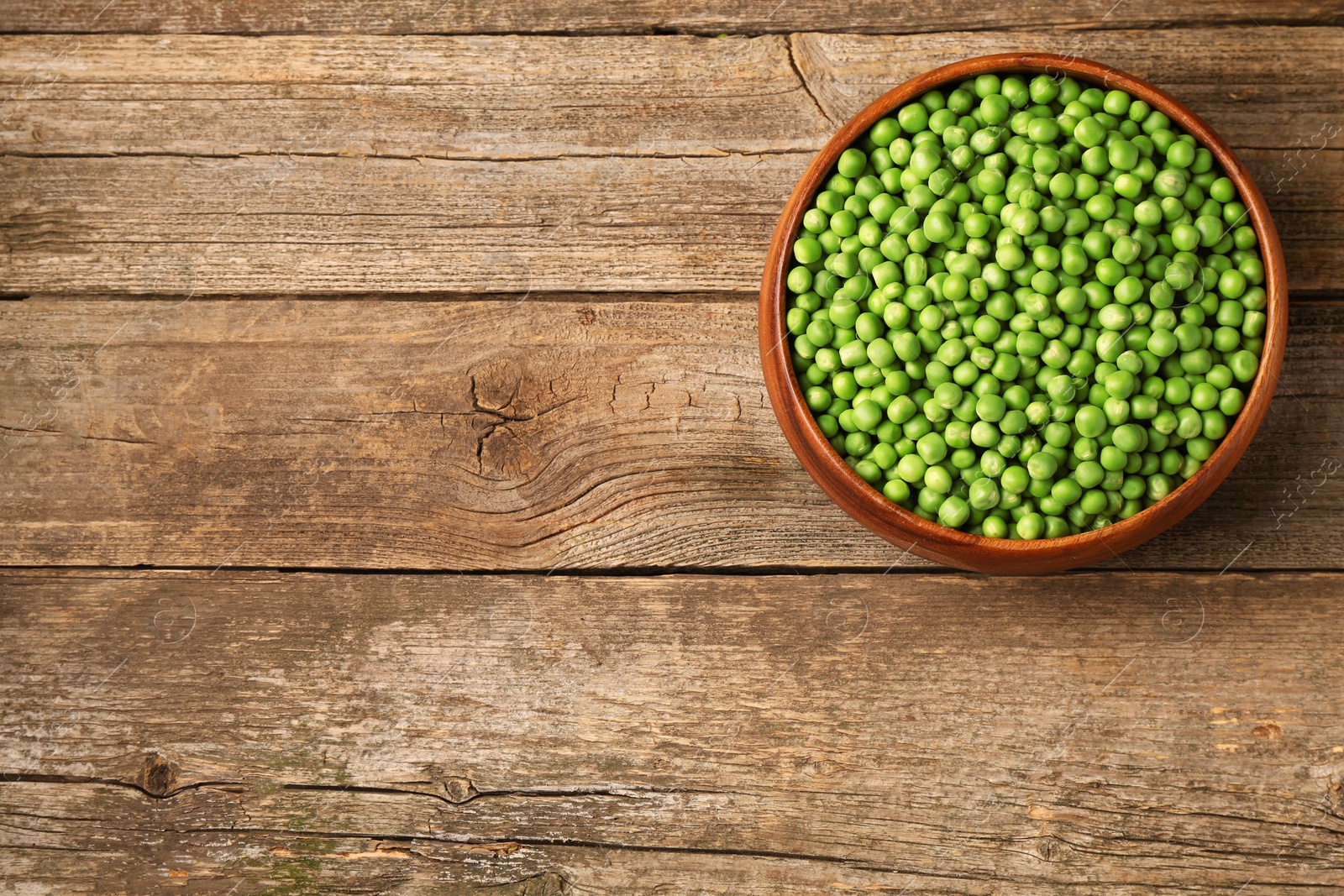 Photo of Fresh green peas in bowl on wooden table, top view. Space for text