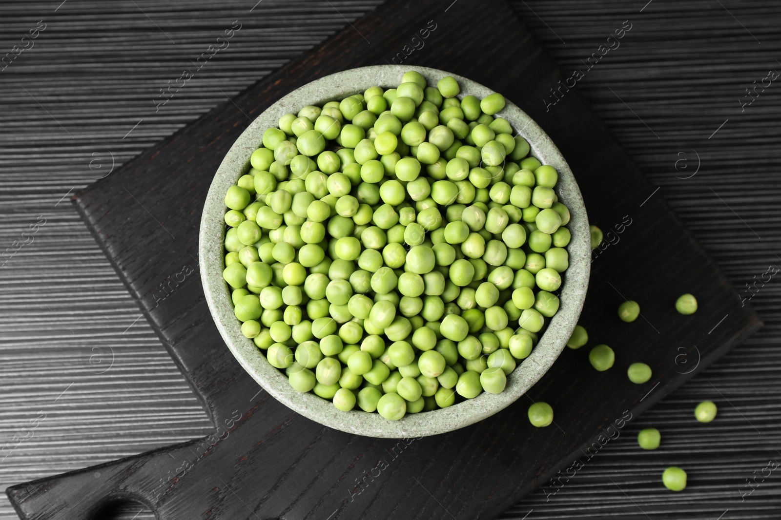 Photo of Fresh green peas in bowl on black wooden table, top view