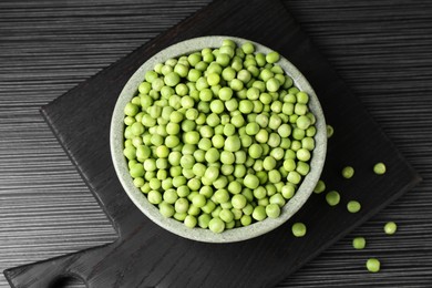 Photo of Fresh green peas in bowl on black wooden table, top view