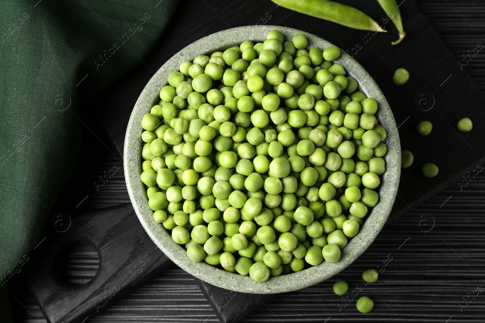 Photo of Fresh green peas in bowl on black wooden table, top view