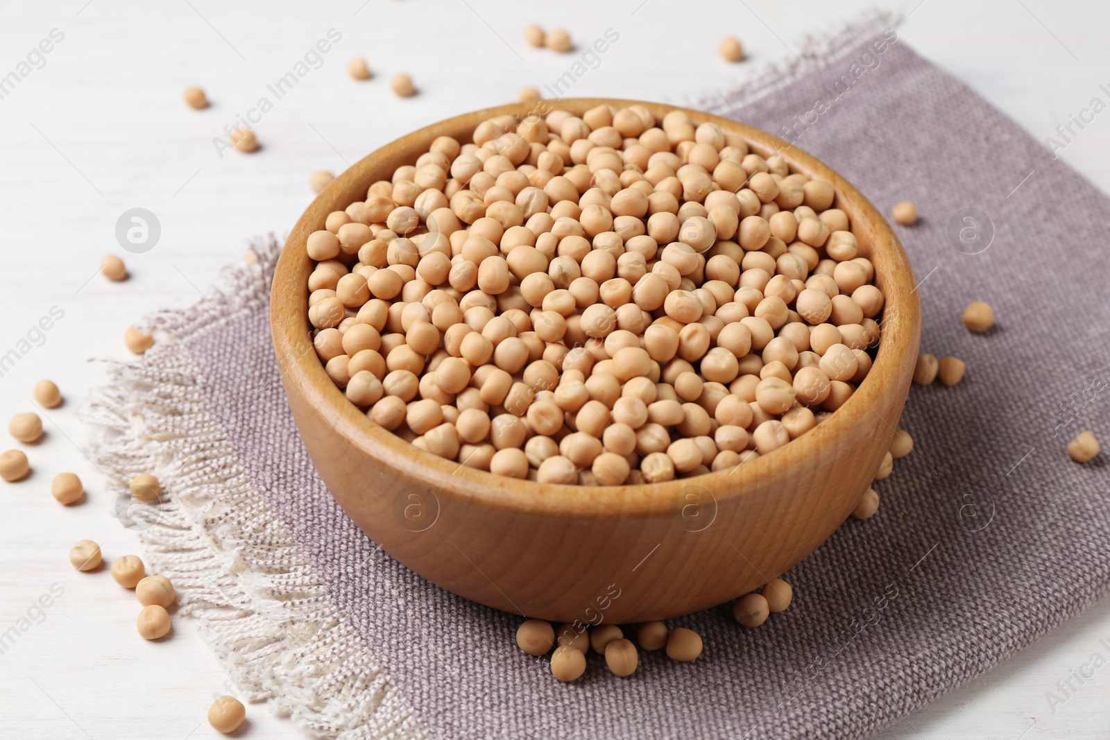 Photo of Dried peas in bowl on light wooden table, closeup