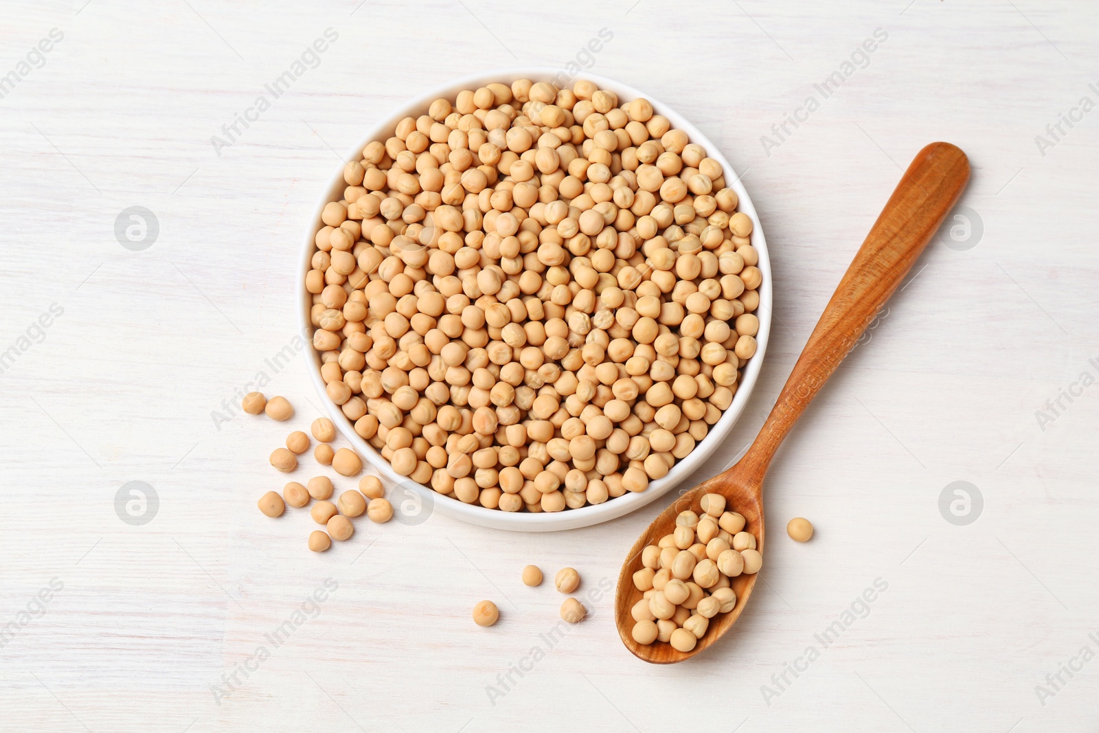 Photo of Dried peas, plate and spoon on light wooden table, flat lay