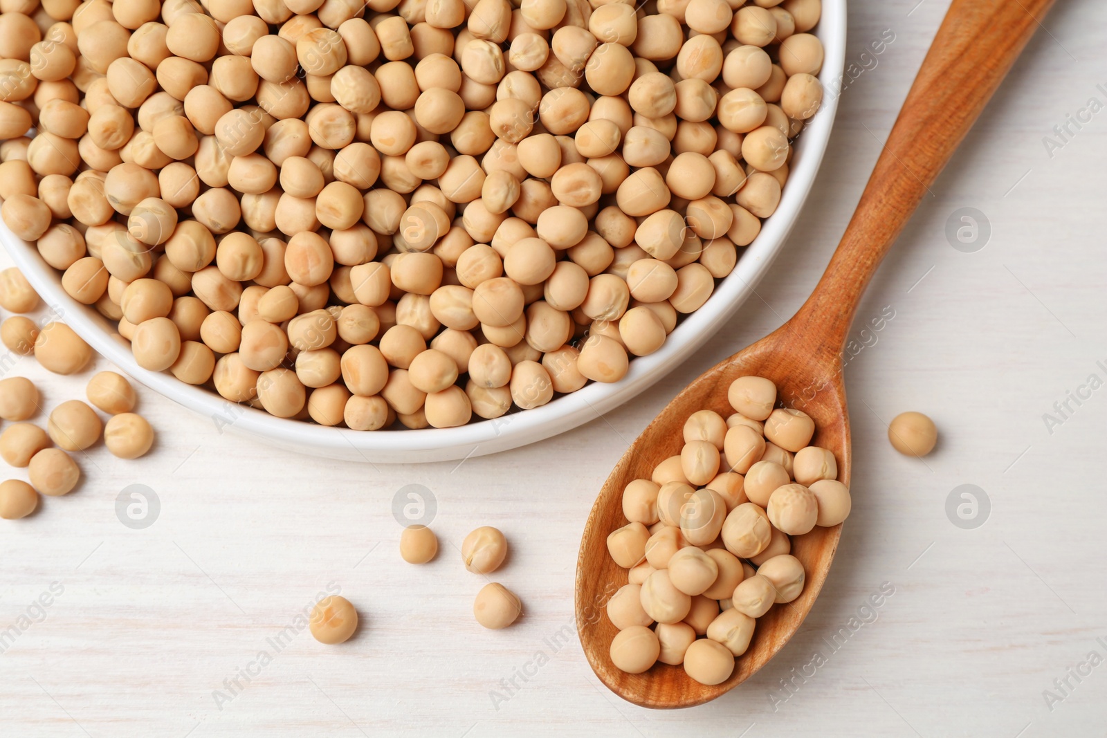 Photo of Dried peas, plate and spoon on light wooden table, flat lay