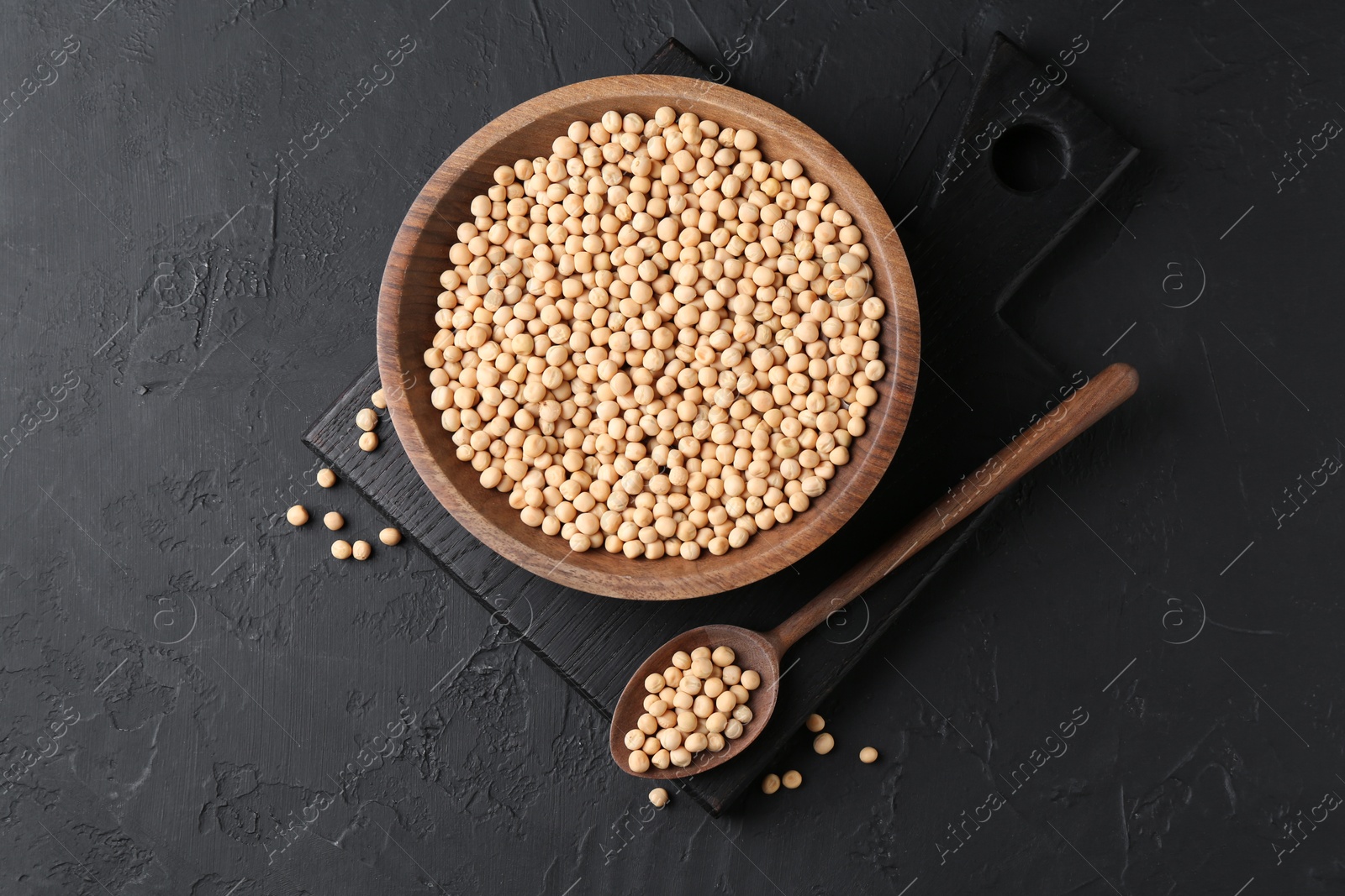 Photo of Dried peas in bowl and spoon on dark textured table, top view