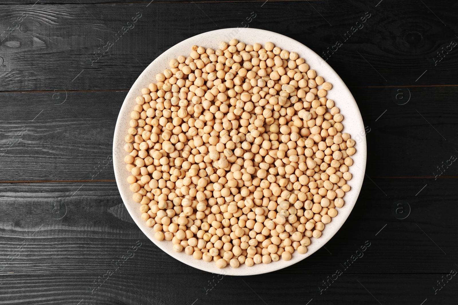 Photo of Dried peas in bowl on black wooden table, top view