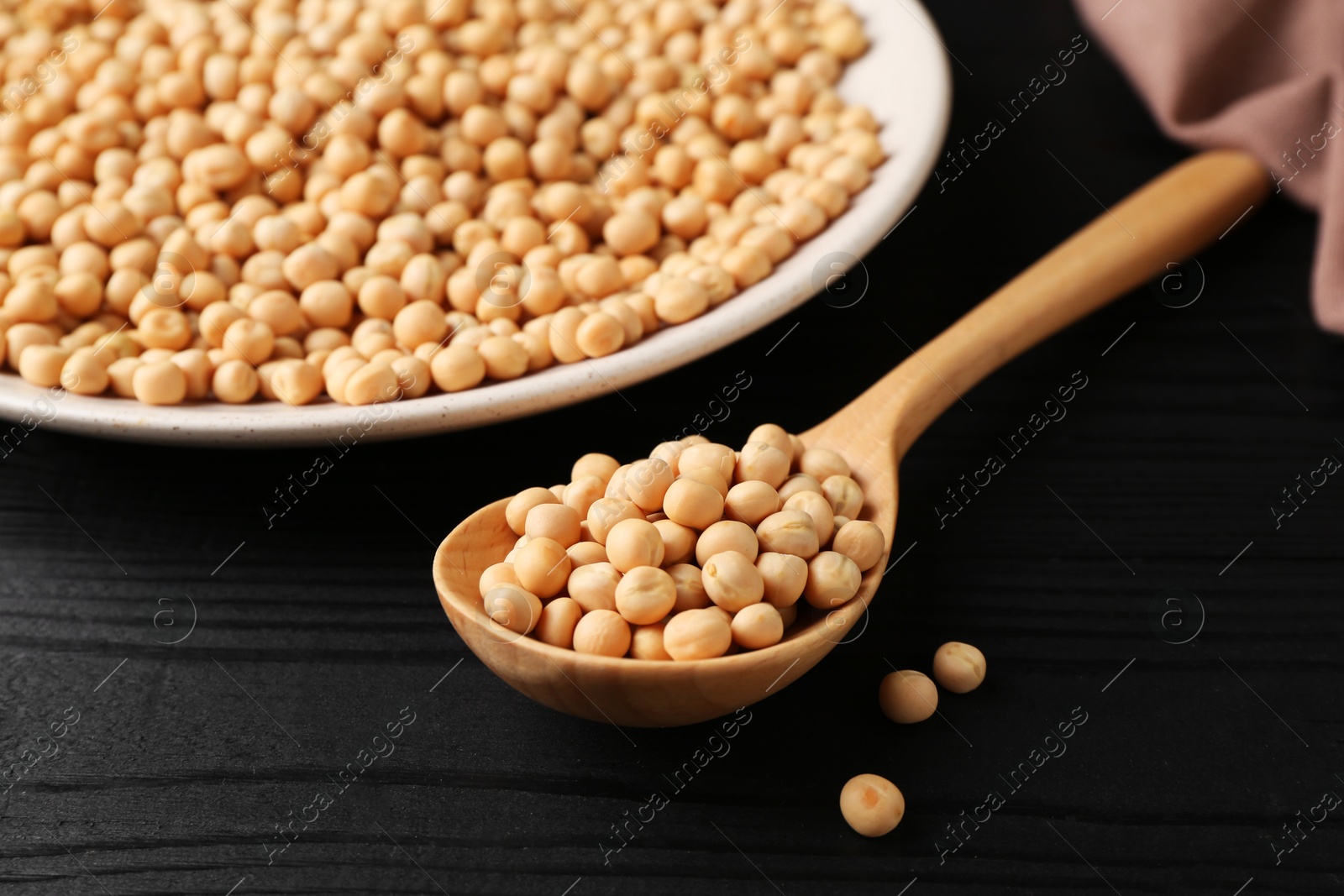 Photo of Spoon with dried peas on black wooden table, closeup