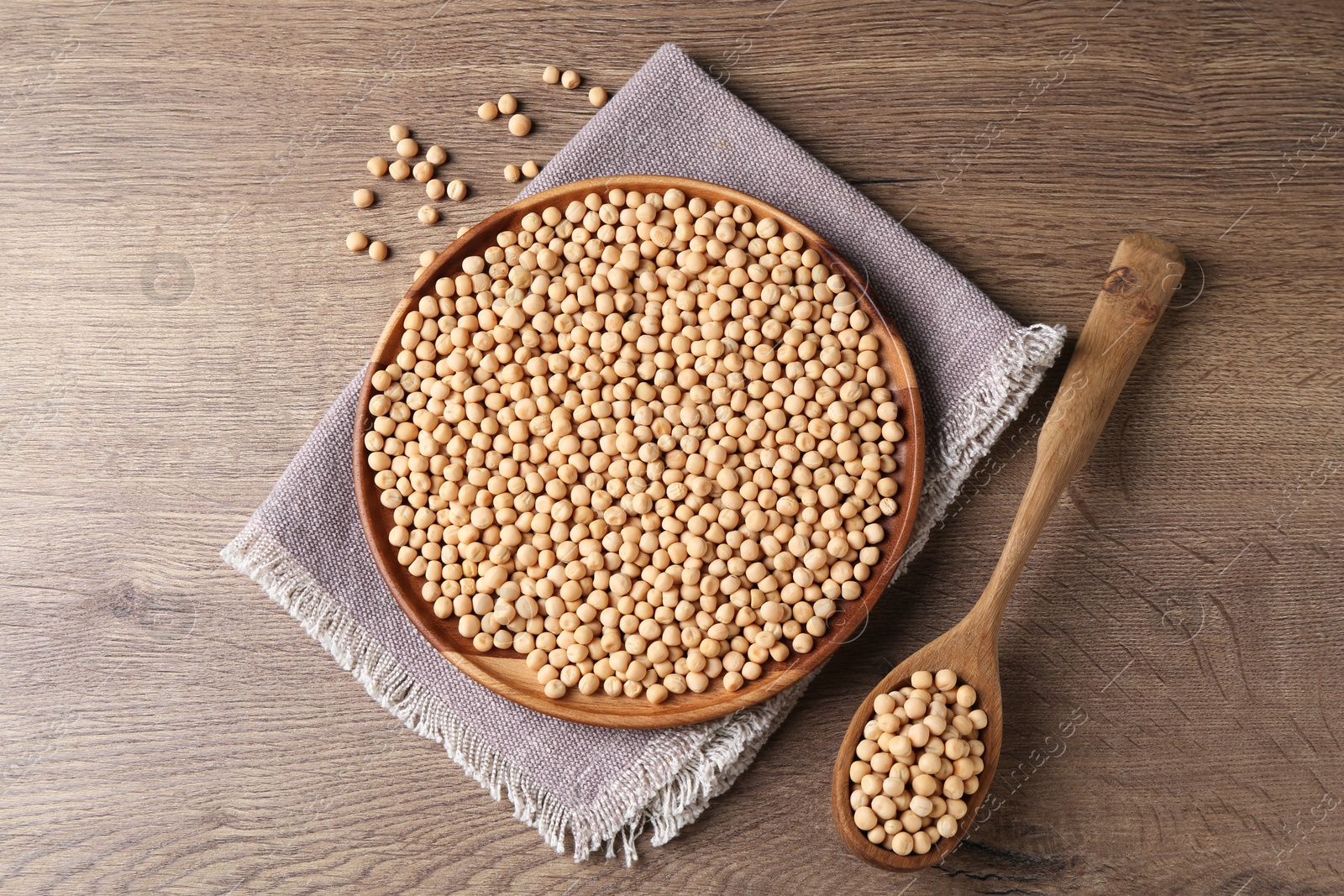 Photo of Dried peas, plate, napkin and spoon on wooden table, flat lay