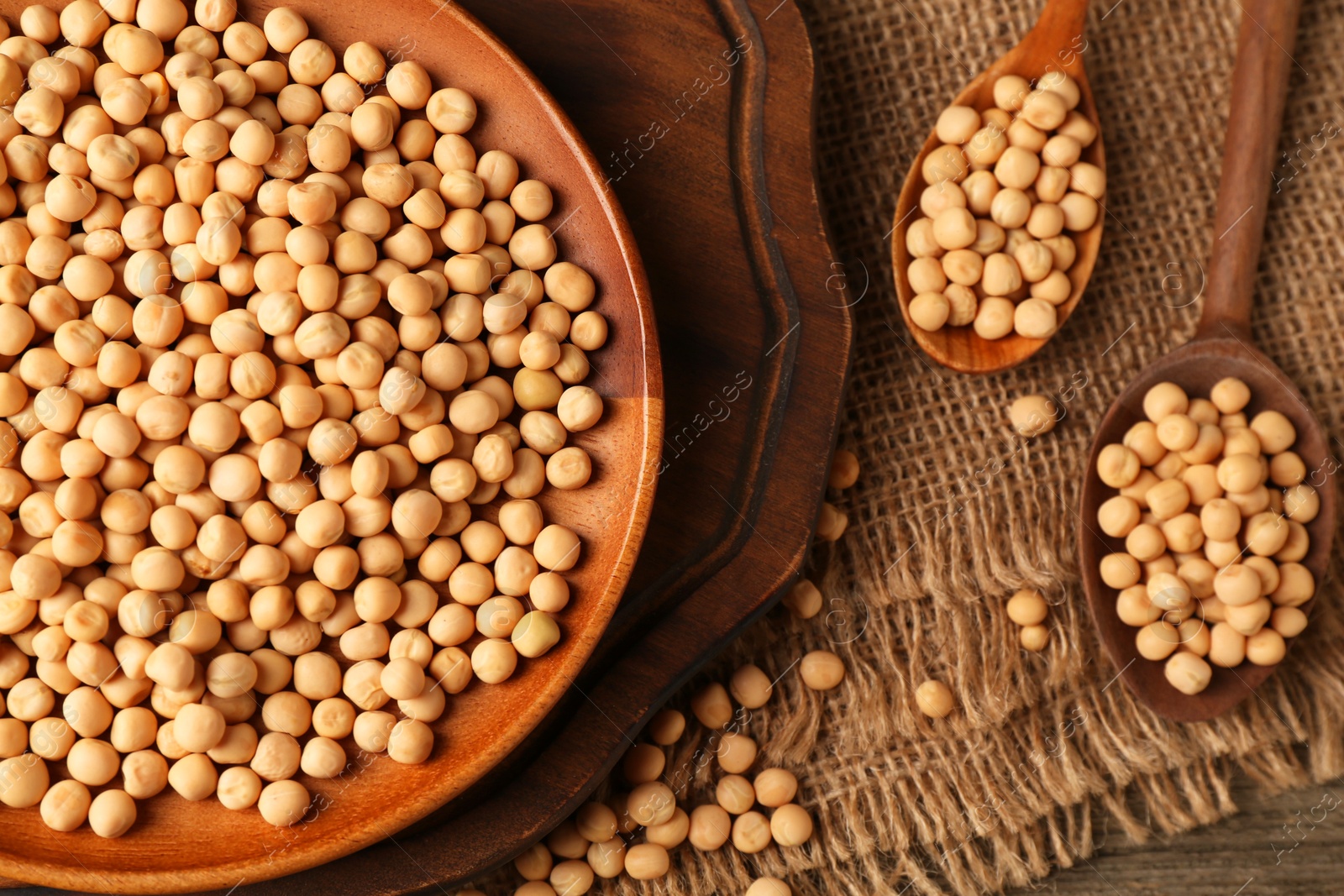 Photo of Dried peas, plate and spoons on wooden table, top view