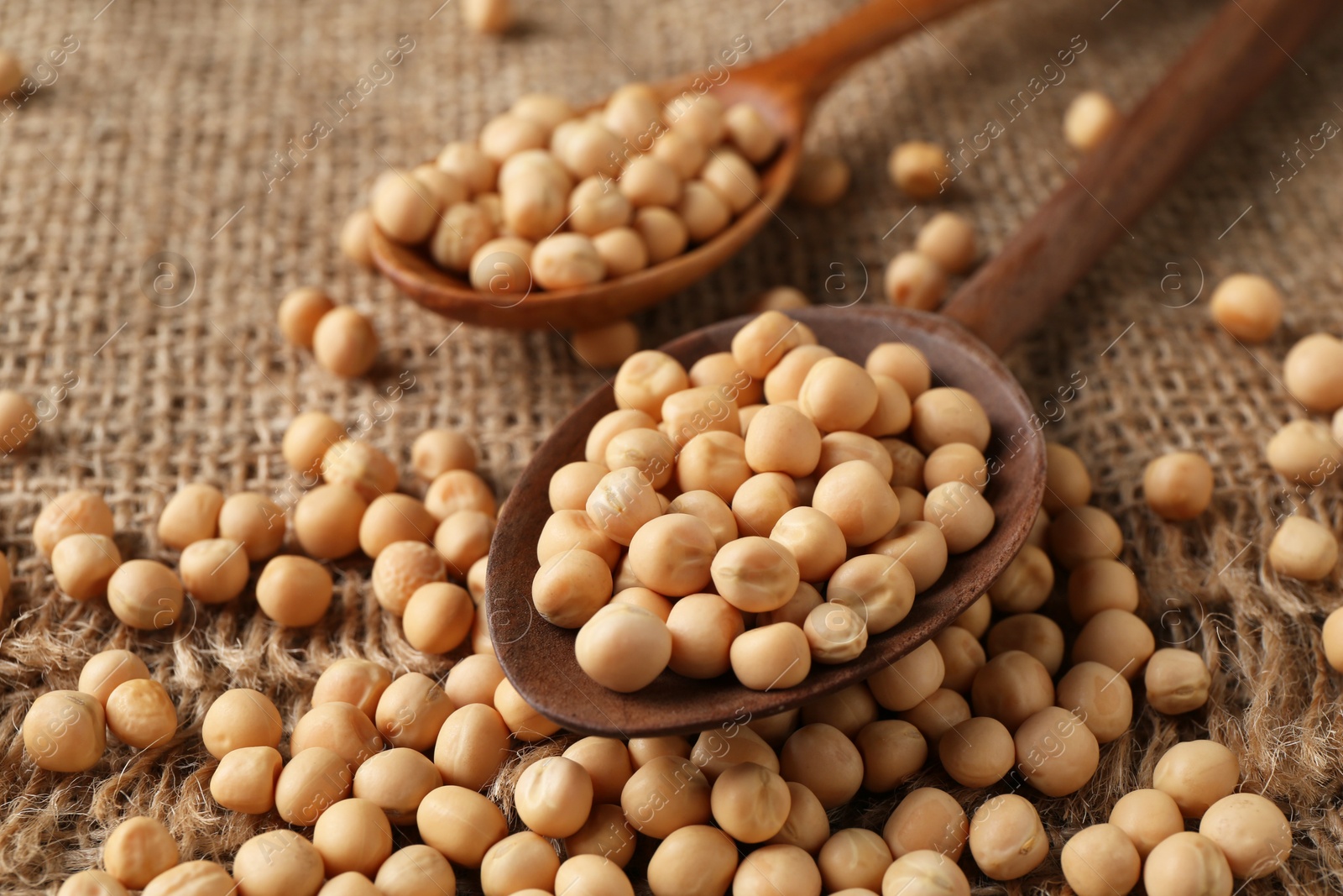 Photo of Spoons with dried peas on burlap fabric, closeup