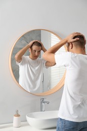 Handsome man looking at mirror in bathroom