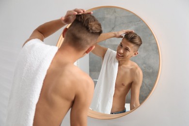 Handsome man with towel looking at mirror in bathroom