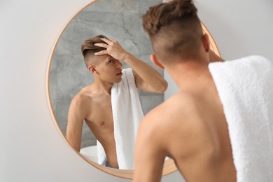 Photo of Handsome man with towel looking at mirror in bathroom