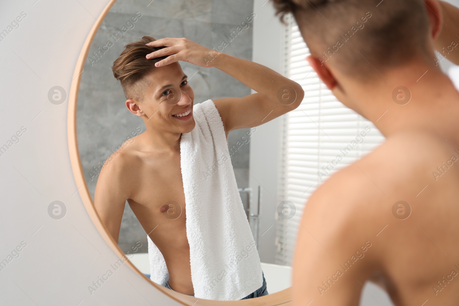 Photo of Handsome man with towel looking at mirror in bathroom