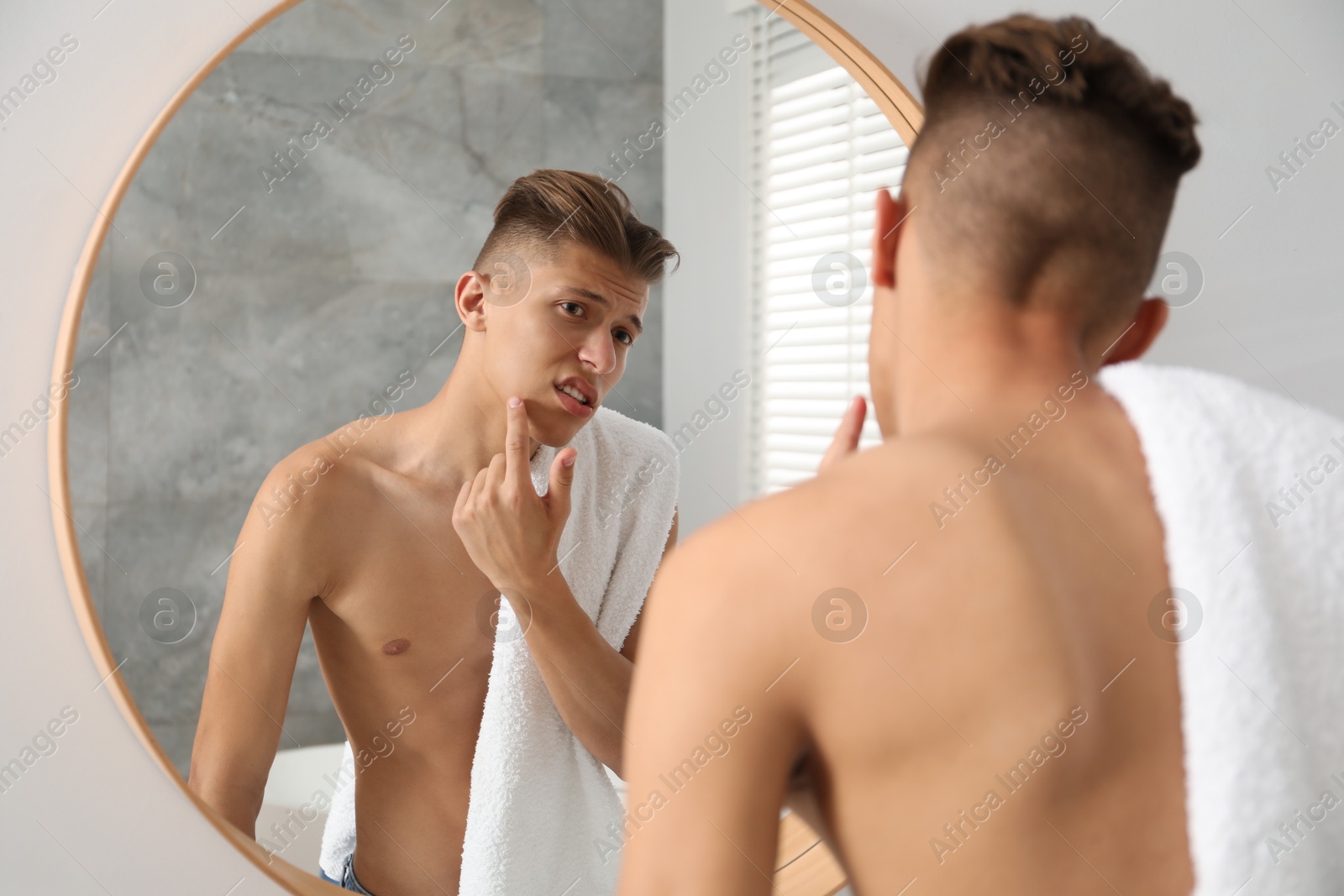 Photo of Man with towel touching his face near mirror in bathroom