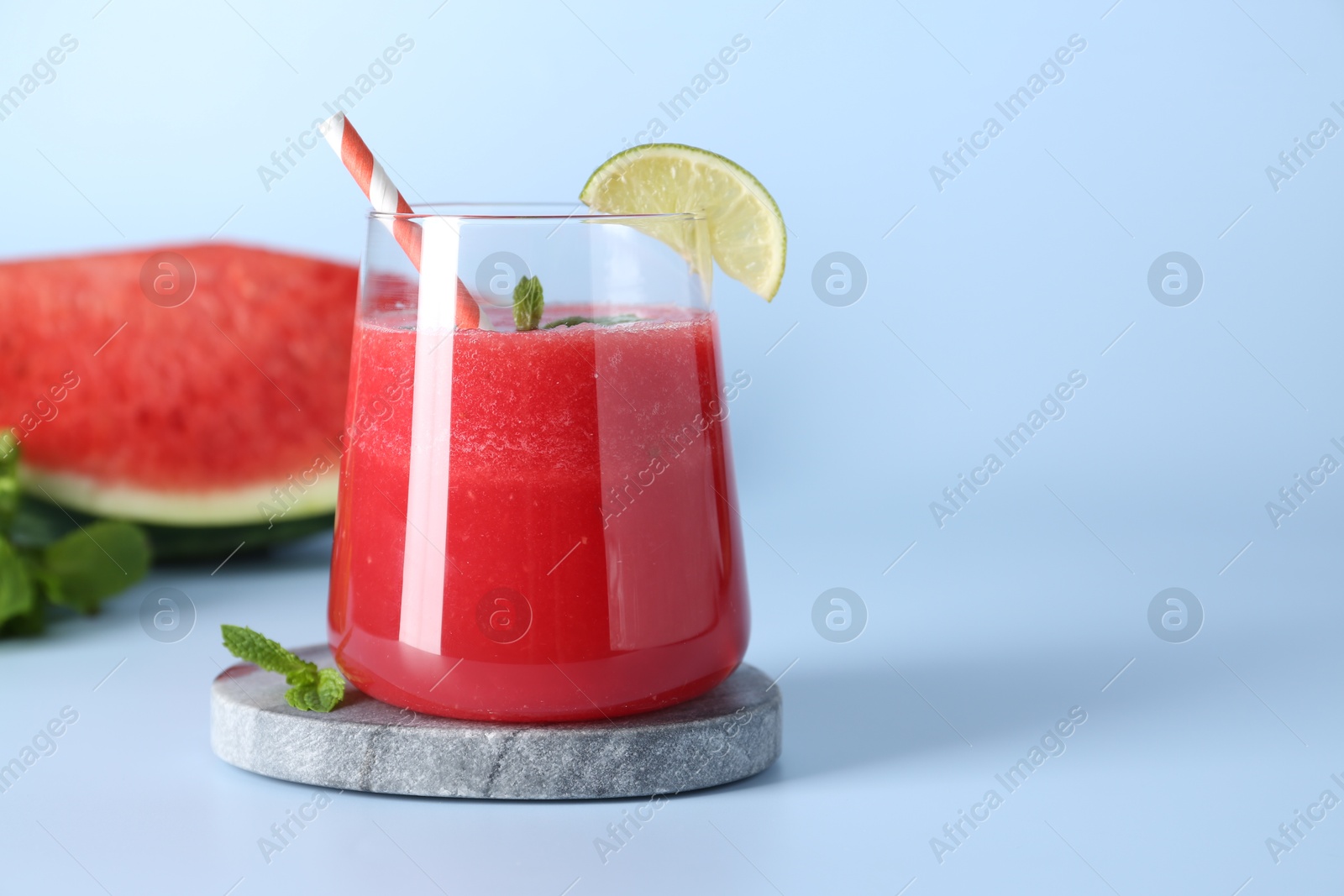 Photo of Tasty watermelon drink in glass, fresh fruits and mint on light blue background, space for text