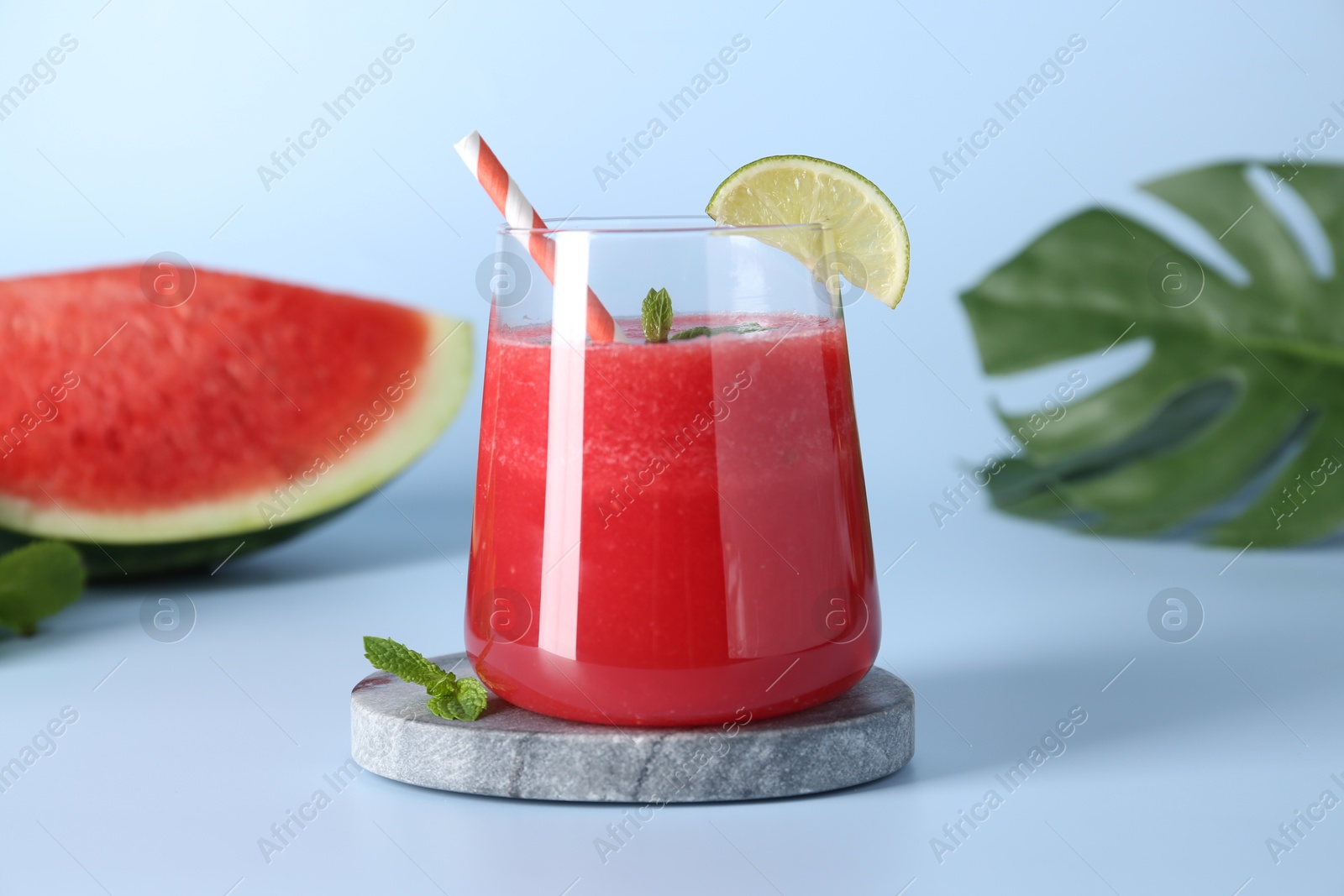 Photo of Tasty watermelon drink in glass, fresh fruits and mint on light blue background