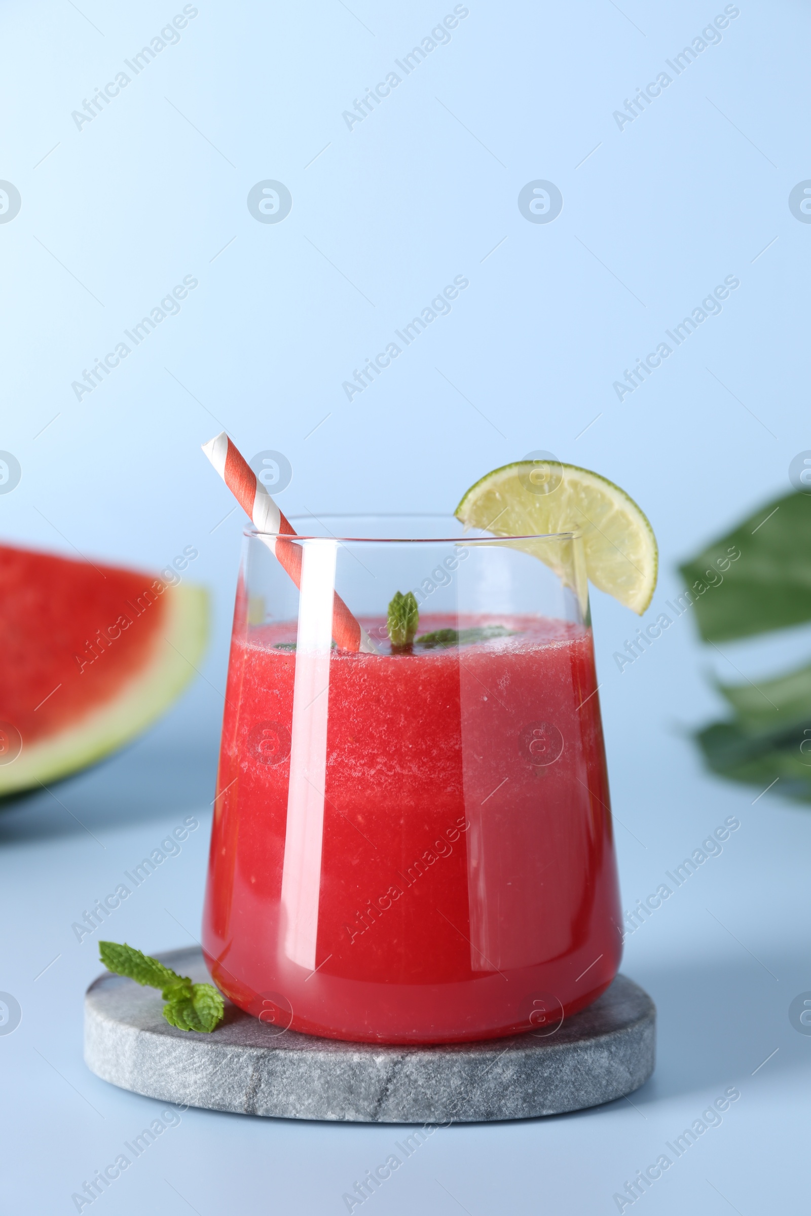 Photo of Tasty watermelon drink in glass, mint and fresh fruit on light blue background