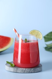 Photo of Tasty watermelon drink in glass, mint and fresh fruit on light blue background