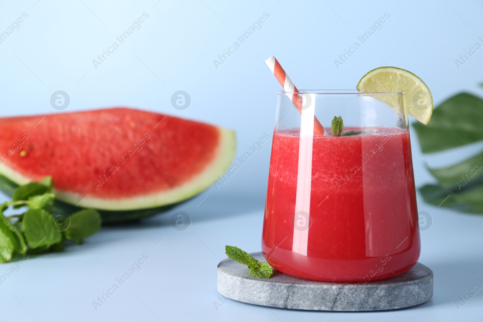 Photo of Tasty watermelon drink in glass, fresh fruits and mint on light blue background, closeup