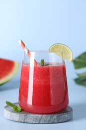 Photo of Tasty watermelon drink in glass, mint and fresh fruit on light blue background, closeup